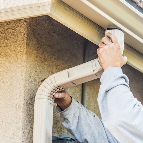 Worker Attaching Aluminum Rain Gutter and Down Spout to Fascia of House